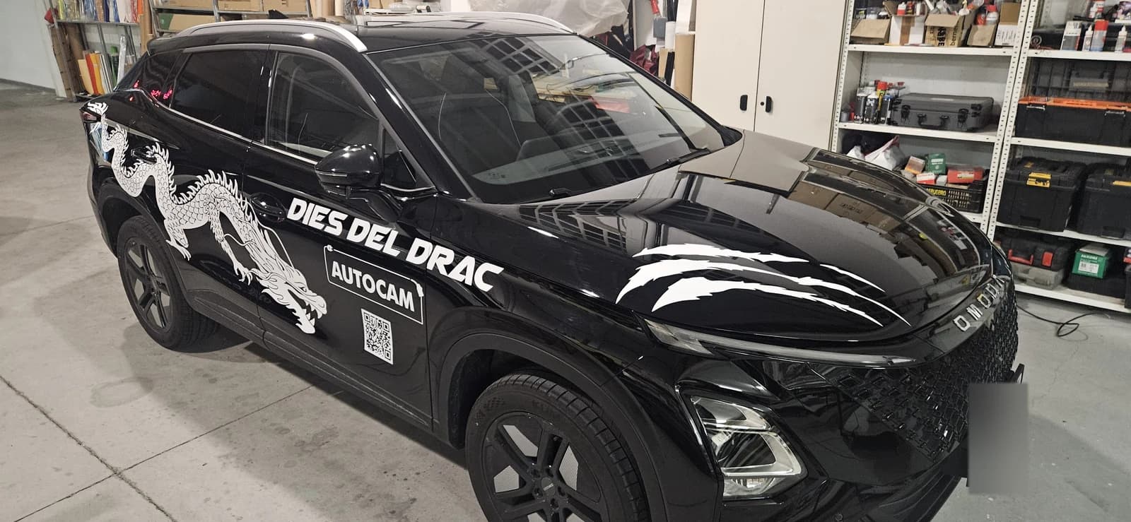 Vista parcial del capó y el lateral con el gráfico blanco del dragón sobre un vehículo negro.