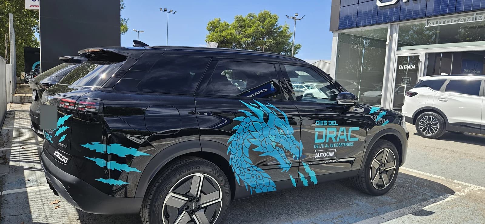 Vista trasera de tres cuartos del vehículo con dragón azul, con continuidad del gráfico sobre la parte trasera.