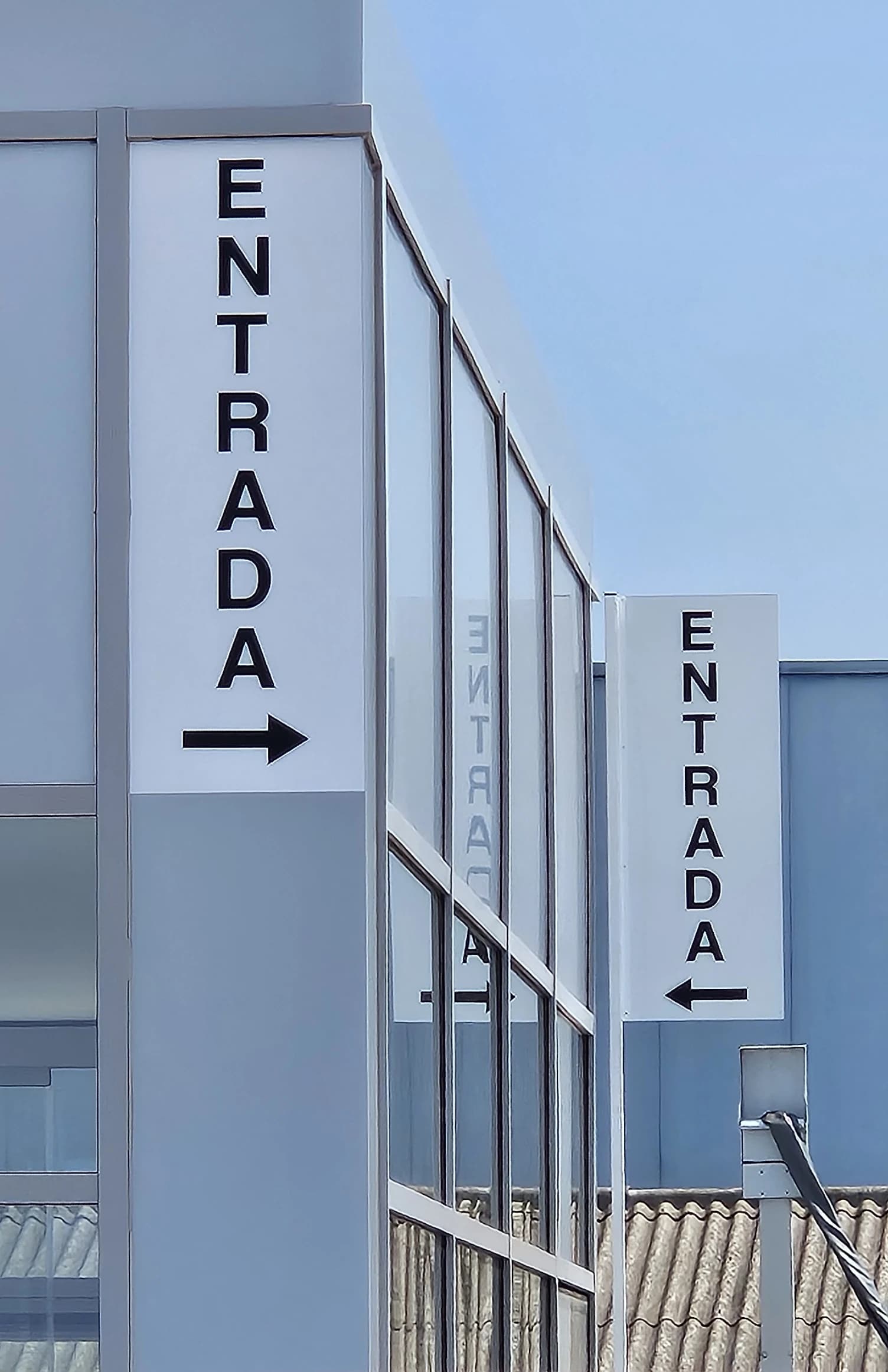 Dos señales verticales de entrada con flechas, en la fachada del recinto.