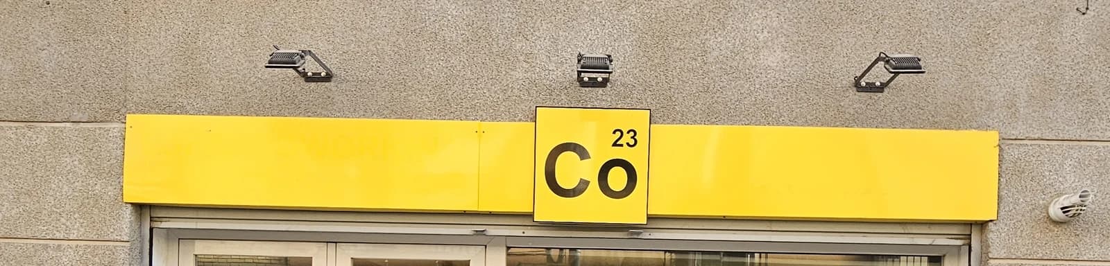 Rótulo amarillo Co23 con tres focos sobre la fachada.