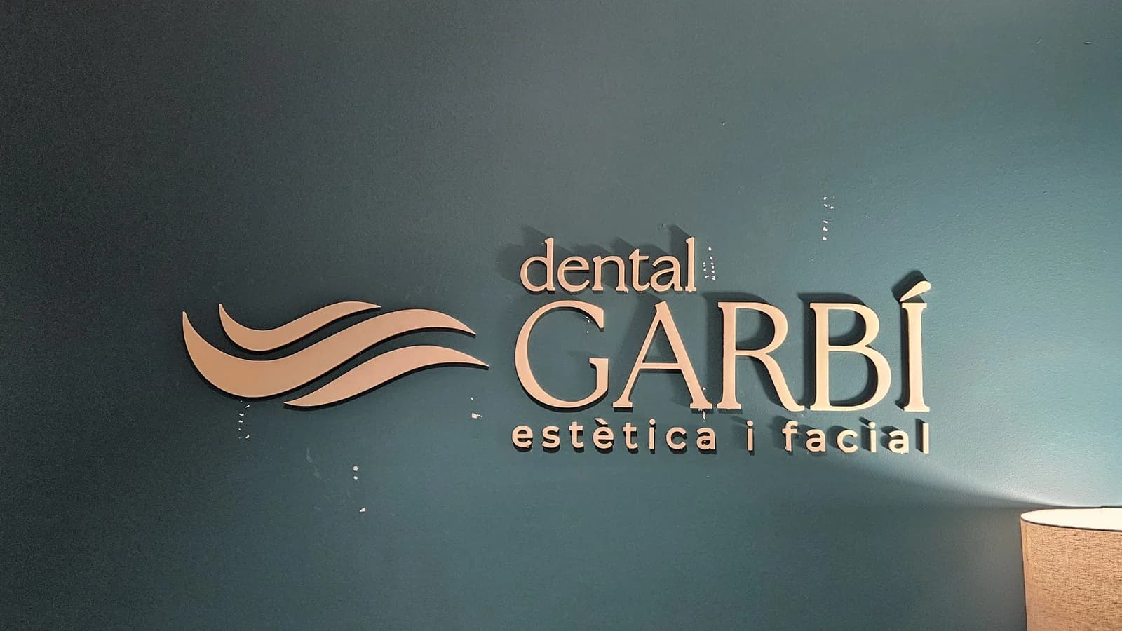Letras y símbolo de Dental Garbí sobre una pared verde.