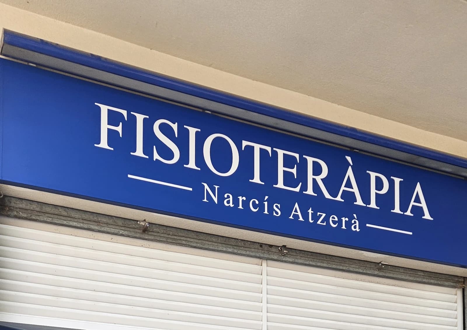 Detalle del rótulo azul de Fisioteràpia Narcís Atzerà sobre la entrada.