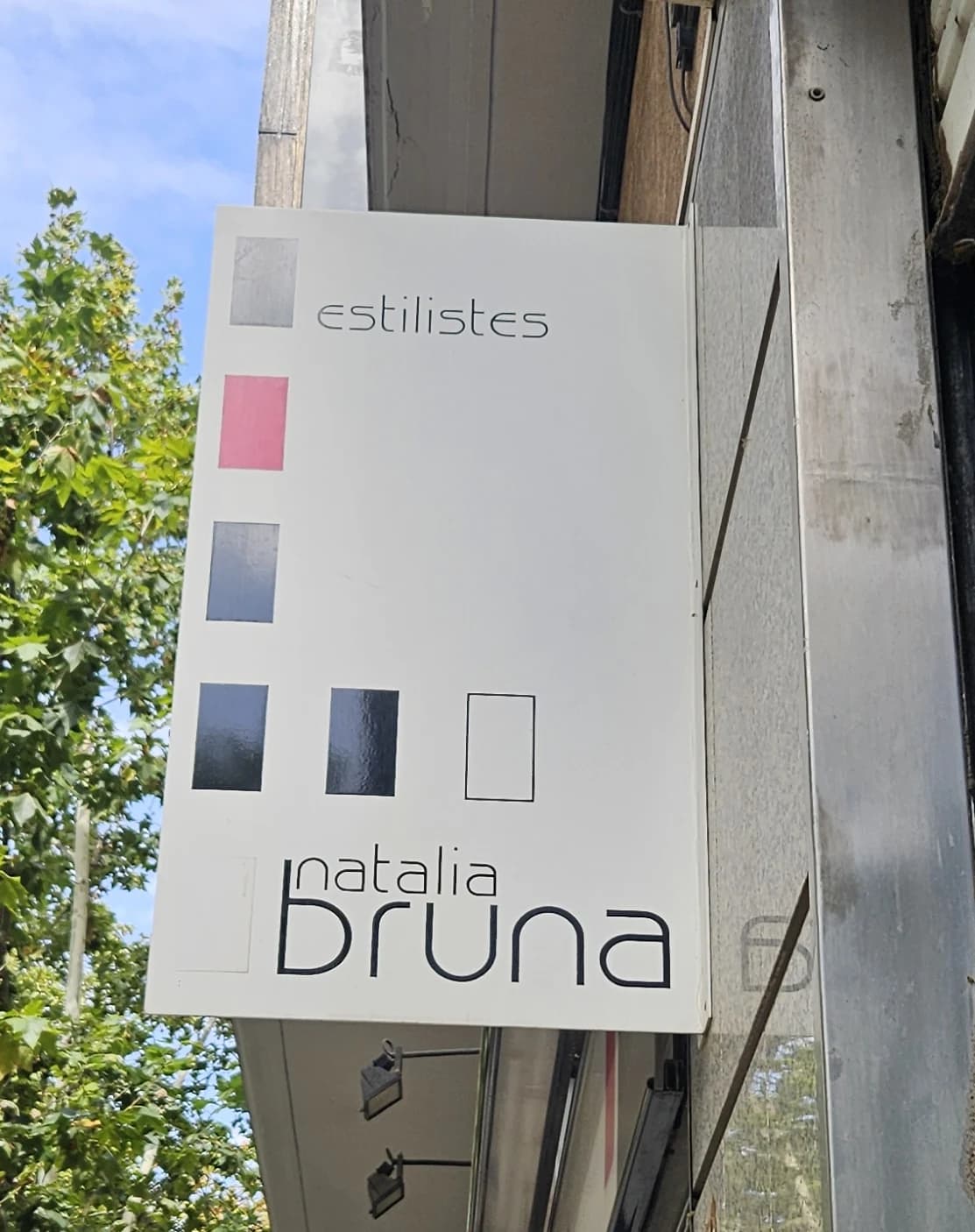 Banderola vertical de Natàlia Bruna vista desde la calle, con el nombre y los cuadrados de colores.