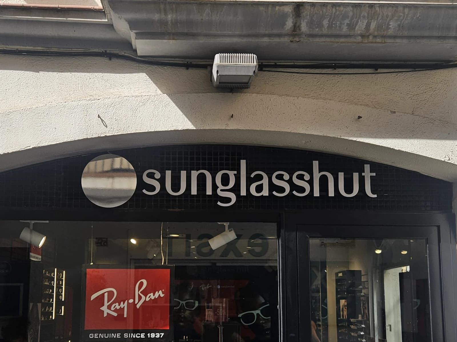 Letras y símbolo de Sunglass Hut sobre el revestimiento negro de la fachada.