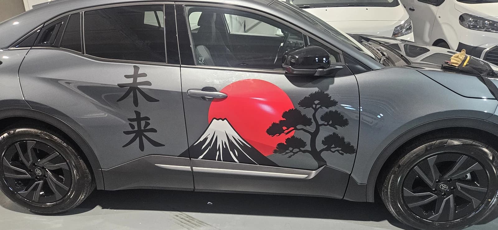 Detalle lateral de vinilo con un sol rojo, un árbol y una montaña sobre las puertas de un Toyota.